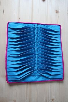 a blue piece of cloth with pink edges on a wooden surface next to scissors and thread