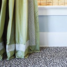 a green curtain with greek border hanging in front of a bathtub and window sill