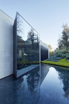 the reflection of trees and bushes in the water is reflected on the glass facade of this modern house