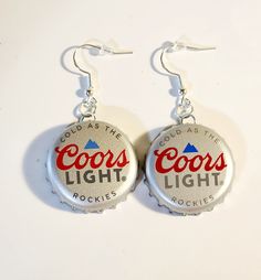 two coca cola bottle caps with the words coors light on them hanging from silver earwires