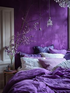 a bed with purple sheets and pillows next to a window