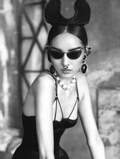 a woman wearing sunglasses and a bow in her hair is sitting on a chair with pearls around her neck