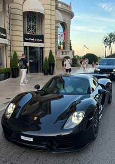 two black sports cars are parked in front of a luxury store with people walking by