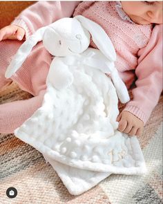 a baby laying on top of a blanket holding a white stuffed animal in it's arms