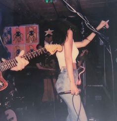 a woman standing in front of a microphone while holding a guitar