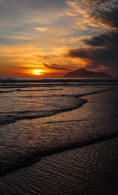 the sun is setting over the ocean with waves coming in to shore and mountains in the distance