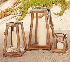 three wooden lanterns sitting on top of a sandy beach next to sea shells and plants