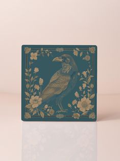 Against a rich emerald backdrop, this ceramic coaster showcases a dignified raven rendered in luminous gold, creating an arresting study in classical naturalist illustration. The deep forest green provides an unexpected sophistication, while metallic botanical elements frame the central figure with remarkable detail. Each carefully composed element, from the raven's precisely articulated feathers to the graceful wildflowers, transforms this functional piece into an artistic statement. ✶ Artisan-crafted ceramic with a protective cork base ✶ Generously sized 3.93" square format ✶ Accommodates both hot and cold beverages ✶ Stabilizing non-slip cork foundation ✶ Simple maintenance with gentle cleaning This distinguished piece resonates with those who appreciate the intersection of artistry and Emerald Backdrop, Cottagecore Kitchen, Academia Aesthetics, Elegant Entertaining, Cart Decor, Bar Cart Decor, Gothic Home, Vintage Botanical Prints, Ceramic Coasters