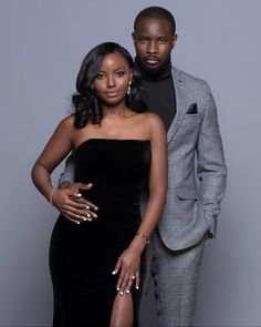 two people standing next to each other in front of a gray background with one person wearing a black dress