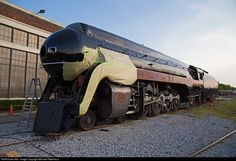 an old train is parked on the tracks near a building with large windows and a yellow tarp covering it's face