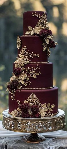 a three tiered red wedding cake with gold flowers on it's side and the top layer is covered in chocolate frosting