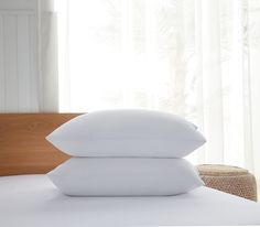 two pillows are stacked on top of each other in front of a bed with white sheets