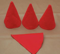 four pieces of red felt sitting on top of a white sheet with three cones and one triangle