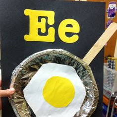 a person holding up a paper plate with an egg on it and the letter e