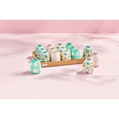 a wooden tray filled with lots of different colored vases and bottles on top of a pink surface