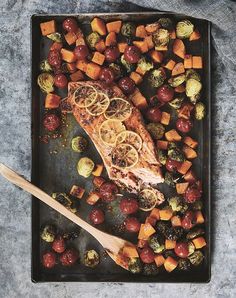 salmon and vegetables on a black tray with a wooden spoon next to it, including brussel sprouts