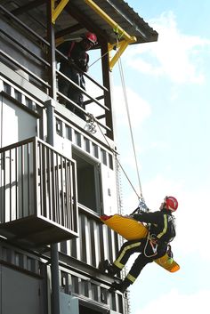 two men in safety gear are hanging from the side of a building while another man is on a rope