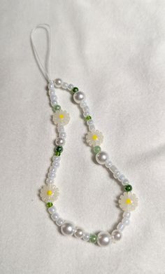 a beaded necklace with flowers and pearls on it's end is laying on a white sheet