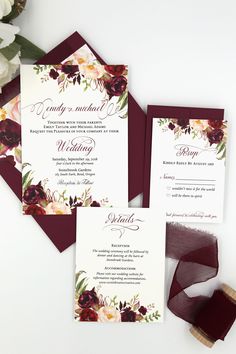 the burgundy and white wedding stationery is set on top of red velvet ribbon, with flowers