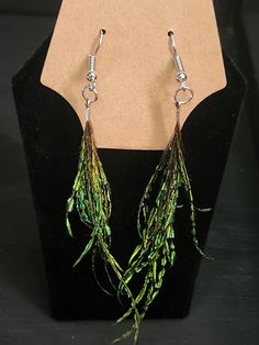 a pair of earrings with green leaves hanging from it's earwires on a black stand