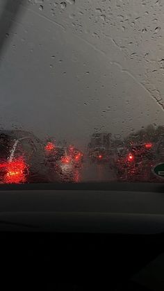 rain is falling on the windshield of a car as traffic lights are seen in the distance