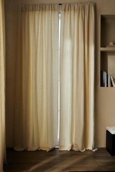 a living room with a large window covered in white curtains and bookshelf behind it