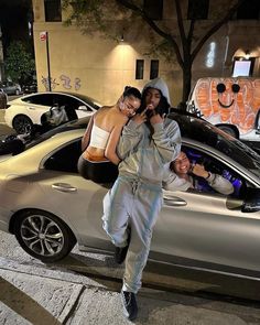 two people standing in front of a silver car