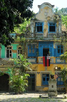 an old building with blue shutters and balconies on the second floor is surrounded by greenery