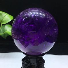 a purple glass ball sitting on top of a black stand next to a green plant