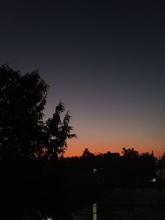 the sun is setting over some trees and buildings in the distance, with no clouds