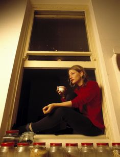 a woman is sitting on the window sill drinking from a cup and looking out