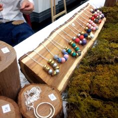 a wooden board with necklaces on it sitting next to other wood logs and moss