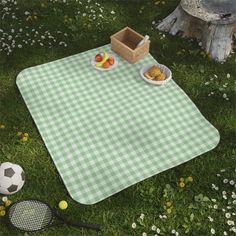 a picnic blanket with food on it sitting in the grass next to a tennis racket