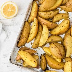 baked potato wedges in a baking dish with lemon and seasoning on the side