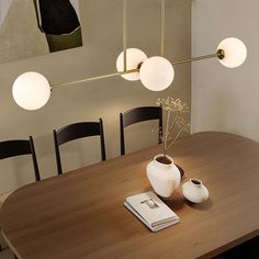 a wooden table topped with two white vases and three lights hanging from the ceiling