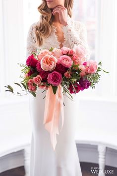 a woman holding a bouquet of pink and red flowers in front of a white wall