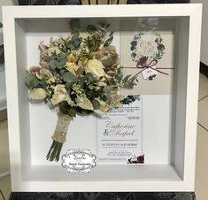 a bouquet of flowers in a white frame on the floor next to a wedding card