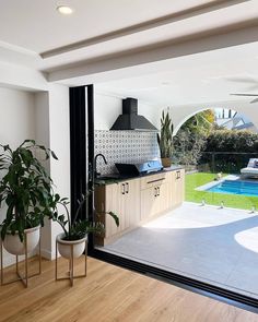 an open kitchen and living room with a pool in the backround, surrounded by potted plants