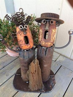 two rusted metal figures with eyes and nose on top of a wooden table next to a potted plant