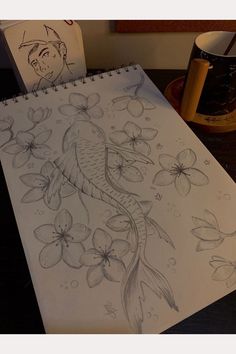 a drawing of a fish and flowers on a table next to a cup with a pen