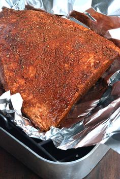 a piece of meat sitting on top of tin foil in a pan next to a wooden table