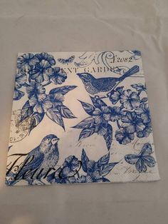 a napkin with blue flowers and birds on it sitting on a white tablecloth covered surface