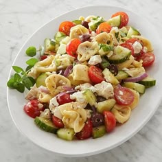 a white bowl filled with pasta salad on top of a marble countertop next to a fork