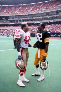 two football players standing next to each other in front of an empty stadium filled with people