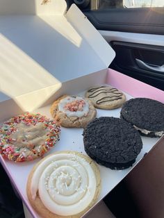 a box filled with lots of different flavored cookies and doughnuts next to a car door