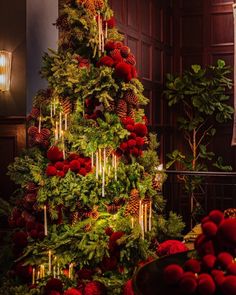 a christmas tree decorated with red balls and pine cones, surrounded by greenery and candles