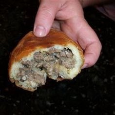 a person holding a piece of bread with meat in it