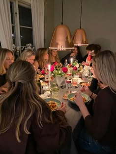 a group of people sitting around a table with plates of food and candles in front of them