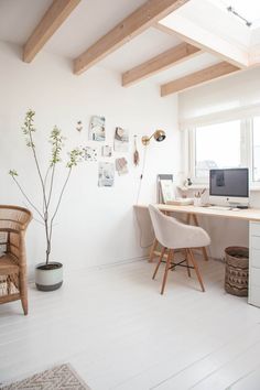 a white room with a desk, chair and computer on the wall next to a potted plant