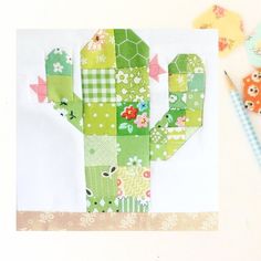 a cactus made out of patchwork paper next to a pen and scissors on a table